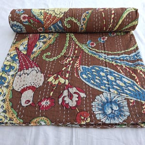 Peut inclure: Couverture kantha marron avec un motif d'oiseaux et de fleurs colorés. La couverture présente des accents rouges, bleus, jaunes et verts. Les bords sont finis avec des coutures blanches. Enroulée en haut.