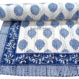 May include: A white cotton kantha quilt with a blue leaf pattern and a blue floral border. The quilt is hand-stitched and has a traditional Indian design. "Kantha Creators" is printed on the quilt.