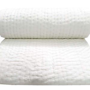 May include: A white, quilted blanket is folded and rolled, with a second blanket unfolded beneath it. The bedding has a textured, grid-like pattern. The background is plain white.