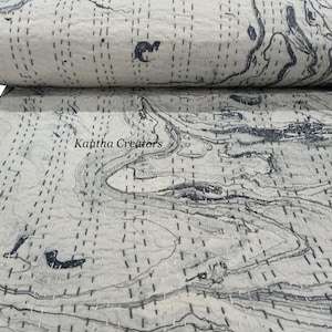 May include: A rolled-up, off-white quilt with a marbled design in shades of gray and black. The quilt features visible stitching throughout and the text "Kantha Creators". This textile is suitable for bedding or decorative use.
