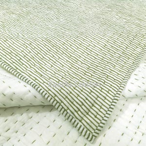 Pode incluir: Um edredom branco e verde-oliva com um padrão listrado. O edredom apresenta um design costurado e um canto dobrado, mostrando os padrões e texturas contrastantes. A roupa de cama é de uma cor suave e neutra.