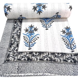 Könnte beinhalten: Weiße Baumwolldecke mit floralem Design in Blau, Grau und Schwarz. Die Decke hat oben einen aufgerollten Abschnitt, der das Muster zeigt. Der Rand hat ein Streifenmuster.