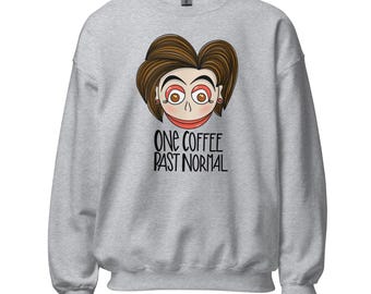 Può includere: Una felpa girocollo grigio chiaro con un'illustrazione a cartone animato di una persona con capelli castani, occhi spalancati e bocca rossa. Sotto l'illustrazione, il testo nero recita: ONE COFFEE PAST NORMAL. Il capo ha maniche lunghe e polsini.