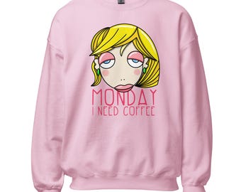Può includere: Una felpa a maniche lunghe rosa chiaro con un'illustrazione a cartone animato di una persona con capelli biondi, palpebre rosa e orecchini verdi. Sotto il viso, il testo MONDAY I NEED COFFEE è scritto in un carattere stilizzato rosso e rosa.
