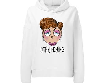 Può includere: Una felpa bianca con cappuccio e maniche lunghe caratterizzata da un'illustrazione grafica di una persona con capelli castani, ombretto rosa ed espressione annoiata. Sotto l'illustrazione, il testo #THATFEELING è stampato in lettere nere.