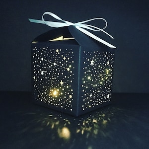 Könnte beinhalten: Eine schwarze Box mit einem weißen Band und einem Sternenmuster. Die Box ist von innen beleuchtet und erzeugt einen Sternenhimmel-Effekt.