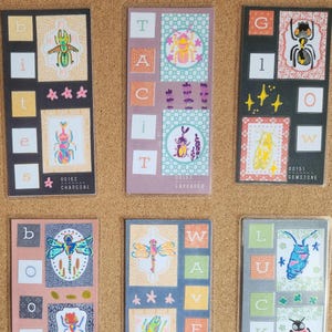 May include: A collection of colorful insect-themed stickers arranged on a corkboard. Each sticker features a different insect illustration, such as beetles, spiders, and dragonflies, with decorative borders and text. The stickers are rectangular and vary in color.