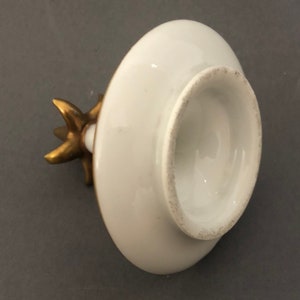 Puede incluir: Tapa de porcelana blanca con un pomo dorado en forma de estrella. La tapa es redonda y tiene una superficie lisa.