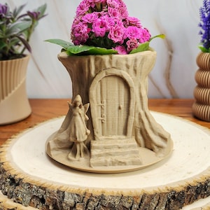 May include: A brown 3D printed planter shaped like a tree stump with a small fairy figurine and a door. The planter is filled with pink flowers and is sitting on a wooden slice.