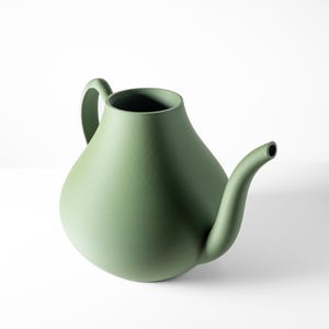 Könnte beinhalten: Eine salbeigrüne Keramik-Gießkanne mit rundem Körper, gebogenem Ausguss und Griff. Die Gießkanne ist mit einem minimalistischen Design gestaltet und eignet sich für den Innen- und Außenbereich. Die glatte Oberfläche und die einzigartige Form machen sie zu einem dekorativen Artikel.