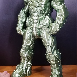 Pu&ograve; includere: Una action figure verde stampata in 3D di un personaggio di un videogioco. La figura &egrave; in piedi con le braccia lungo i fianchi e indossa un'armatura dettagliata.