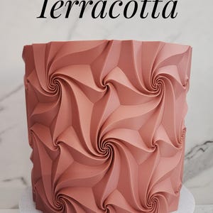 May include: A cylindrical terracotta-colored object featuring a repeating geometric pattern of swirling, raised ridges that create a vortex-like effect across the surface. The word Terracotta is printed in black text above the object.