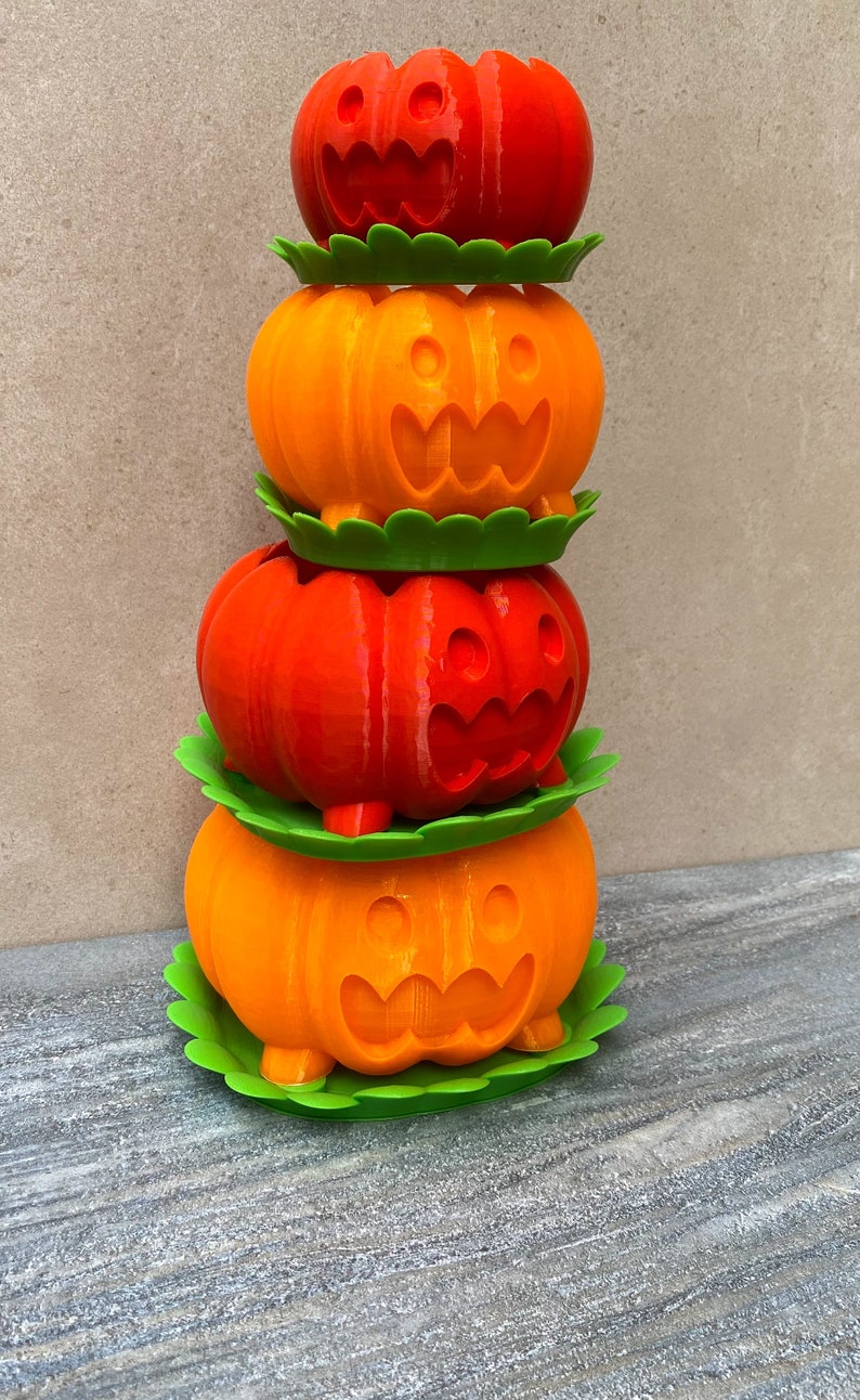Peut inclure: Une pile de quatre pots en forme de citrouille orange et rouge avec des bases feuillues vertes. Chaque pot a un visage de citrouille sculpt&eacute;.