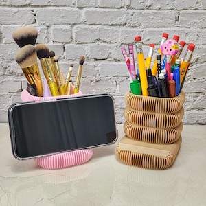 May include: A pink and beige desk organizer set. The pink organizer holds makeup brushes and a smartphone. The beige organizer holds pens, pencils, and markers. The organizers have a ribbed design.