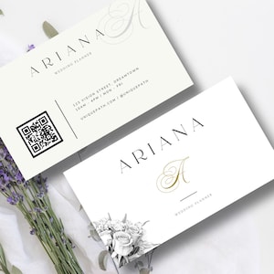 Op de afbeelding: Twee witte visitekaartjes met zwarte tekst. De bovenste kaart heeft een zwart-witte QR-code en de tekst "ARIANA WEDDING PLANNER 123 VISION STREET, DREAMTOWN 10AM - 4PM / MON - FRI UNIQUEPATH.COM / @UNIQUEPATH". De onderste kaart heeft een zwart-wit bloemenpatroon in de linkerbenedenhoek en de tekst "ARIANA A WEDDING PLANNER".