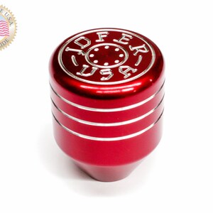 Puede incluir: Pomo de cambio de marchas de aluminio rojo con un logotipo JOFER USA plateado y tres anillos plateados alrededor de la base.