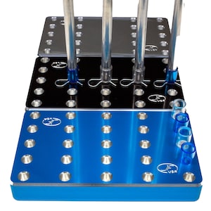 May include: A blue metal stand with multiple holes for holding tools. The stand has a black metal plate and a silver metal plate stacked on top of it. There are four silver rods with blue caps inserted into the top plate.