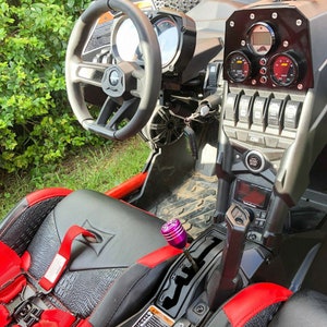 Puede incluir: El interior de un veh&iacute;culo todoterreno rojo y negro con una palanca de cambios de color p&uacute;rpura, un asiento de cuero negro con costuras rojas y un tablero con varios indicadores y interruptores.