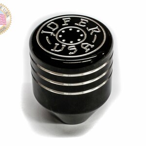 Puede incluir: Pomo de cambio negro con detalles plateados y las palabras "OFF" y "ER" en la parte superior. El pomo tiene tres anillos plateados alrededor del medio.