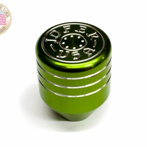 Puede incluir: Pomo de cambio de marchas de metal verde con un logotipo 'JOFER USA' plateado y tres anillos plateados alrededor del centro.