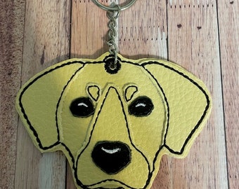 May include: A yellow felt dog head keychain with black embroidered eyes, nose, and mouth. The keychain is attached to a silver metal key ring.