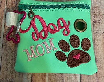 May include: Green zippered pouch with a brown paw print and the text "Dog Mom" in pink embroidery. The pouch has a metal ring and a pink carabiner clip.