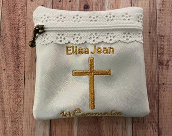 May include: White fabric pouch with a zipper closure and lace trim. The pouch is embroidered with the name "Elisa Jean", a gold cross, and the text "1st Communion".