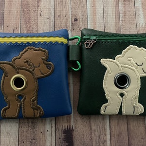 May include: Two dog poop bag holders, one blue with a brown dog and one green with a cream dog. Both have a zipper closure and a metal ring.