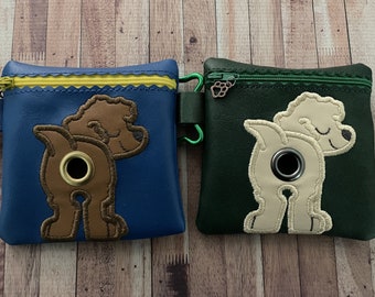 May include: Two dog poop bag holders, one blue with a brown dog and one green with a cream dog. Both have a zipper closure and a metal ring.