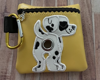 May include: A yellow dog poop bag holder with a black and white dalmatian dog design. The holder has a zipper closure and a metal clip.