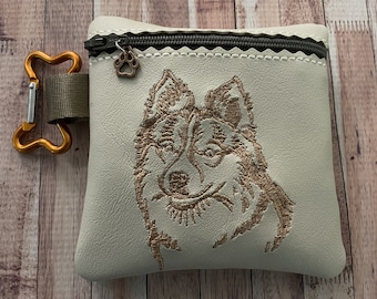 May include: A white zippered pouch with a brown embroidered dog design. The pouch has a brown paw print charm attached to the zipper.