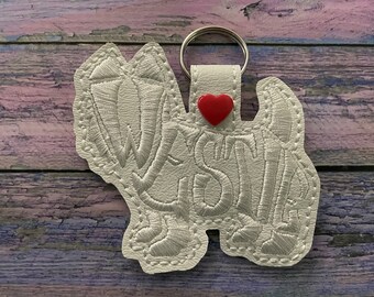 May include: White leather keychain with the word "Westie" embroidered in white thread and a red heart charm.