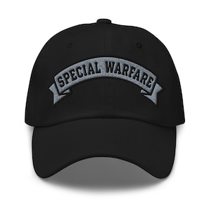 May include: Black baseball cap with the words "SPECIAL WARFARE" embroidered in gray across the front. The text is arched on a gray banner. The cap has a curved brim and a button on top.