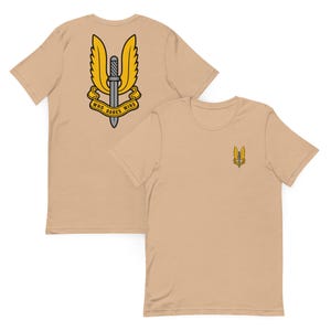 May include: A tan short-sleeved t-shirt featuring a small graphic on the front left chest and a large version of the same graphic on the back. The graphic depicts a grey sword with yellow wings and a yellow banner with the text WHO DARES WINS.