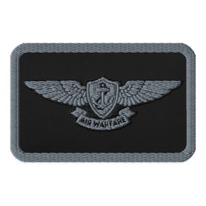 May include: A rectangular embroidered patch with a black background and a grey border. The centre features a grey embroidered emblem of wings flanking a shield containing an anchor, with a banner below the shield reading AIR WARFARE.