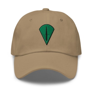 Puede incluir: Gorra de béisbol beige con visera curva. Presenta un emblema bordado en verde y negro en la parte delantera, con forma de diamante y una línea vertical. Cierre de correa de tela ajustable.