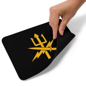 May include: Black rectangular mousepad featuring a gold trident, lightning bolt, and sword design. The mousepad has a black textured surface on the bottom and a smooth black surface on top. The design is centered on the mousepad.