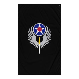 Op de afbeelding: Een zwarte vlag met een wit gevleugeld embleem. Het embleem heeft een blauwe cirkel met een witte ster en een rood centrum. Een zilveren dolk met een gouden handvat is gecentreerd in de vleugels.