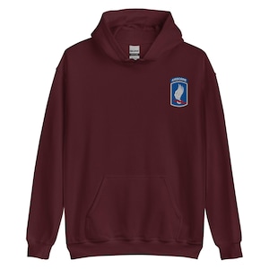 May include: A maroon hoodie with a kangaroo pocket and a drawstring hood. The upper right chest features a patch with the word "AIRBORNE" above a white winged design on a blue background.