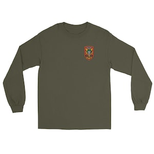 May include: An olive green long-sleeved shirt with a small embroidered patch on the upper left chest. The patch features a skull, a sword, and other military-themed imagery in red, yellow, and green. The shirt has a crew neck and long sleeves.