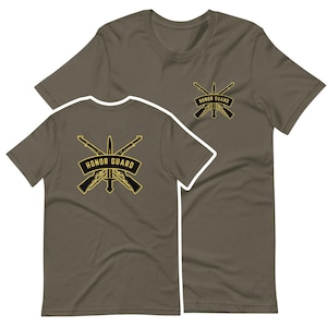 May include: Two olive green t-shirts with a gold graphic of crossed rifles and a bayonet with the text "Honor Guard" on a banner.