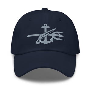 May include: A navy blue baseball cap with an embroidered anchor, gun, and trident in silver gray.