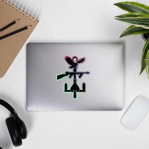 Puede incluir: Una pegatina con la silueta negra de un águila, un rifle y un ancla. El diseño está sobre un fondo blanco con un degradado de rosa y verde.
