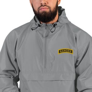 May include: A gray hooded jacket with a half-zip closure and a black drawstring. The jacket features a yellow and black "RANGER" patch on the chest. The jacket is made of a lightweight material.