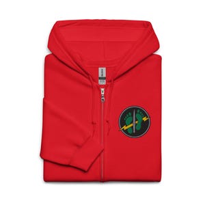 May include: A bright red zip-up hoodie featuring a circular embroidered patch on the left chest. The patch displays two green footprints, a silver dagger positioned vertically between them, and a yellow lightning bolt crossing the design horizontally.