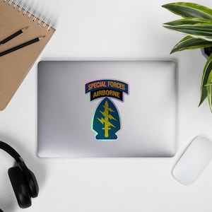 May include: A sticker featuring the Special Forces Airborne insignia. The design includes a blue and yellow arrowhead with lightning bolts and the words "SPECIAL FORCES AIRBORNE" in a banner.