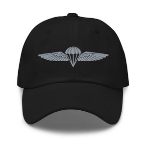 Peut inclure: Une casquette de baseball noire avec un design d'ailes de parachute brodé en gris.