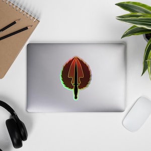 May include: A holographic sticker featuring a black silhouette of a dagger with a red, orange, and yellow gradient background.