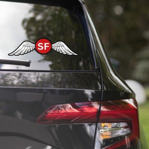May include: A black car with a red circle sticker on the back window. The sticker has white wings and the letters "SF" in white inside the circle.