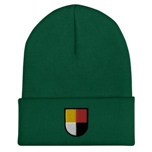 May include: A green beanie with a colourful embroidered patch featuring a shield with yellow, red, white and black sections.
